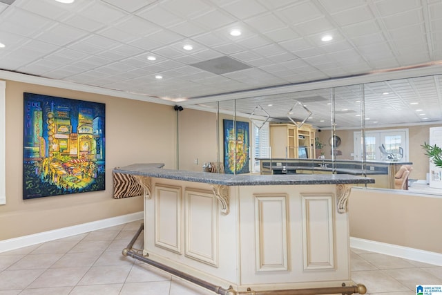 bar featuring light tile patterned floors, crown molding, dark stone counters, and cream cabinets