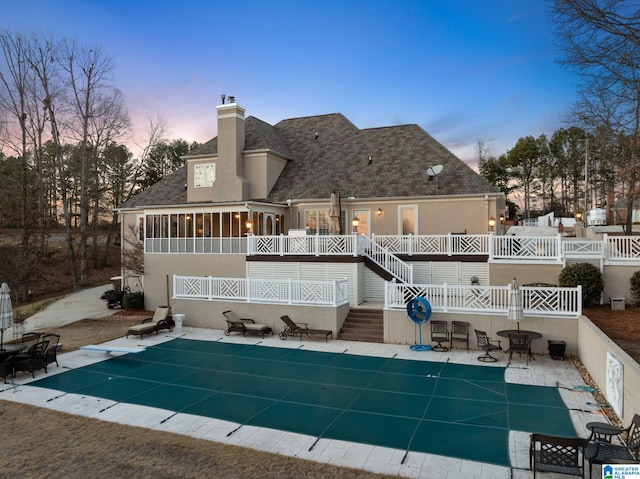 back house at dusk featuring a sunroom, a patio area, and a covered pool