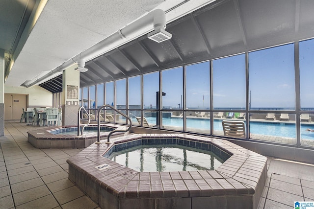 view of pool with an indoor hot tub and a water view