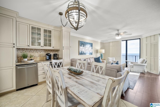 dining room with floor to ceiling windows, a water view, light tile patterned floors, ceiling fan with notable chandelier, and ornamental molding