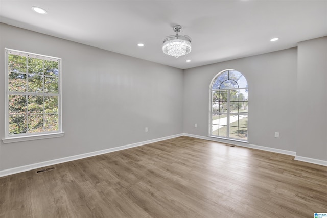 empty room with hardwood / wood-style flooring, an inviting chandelier, and a healthy amount of sunlight