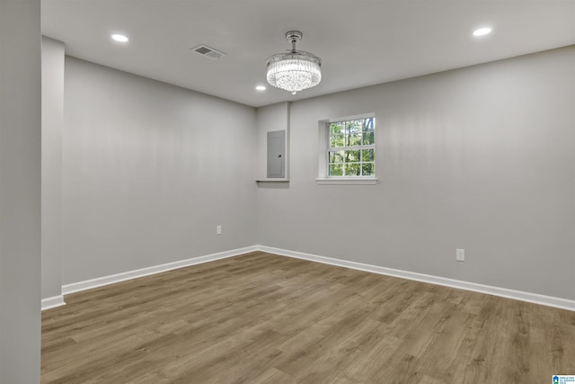 spare room featuring hardwood / wood-style floors, electric panel, and a chandelier