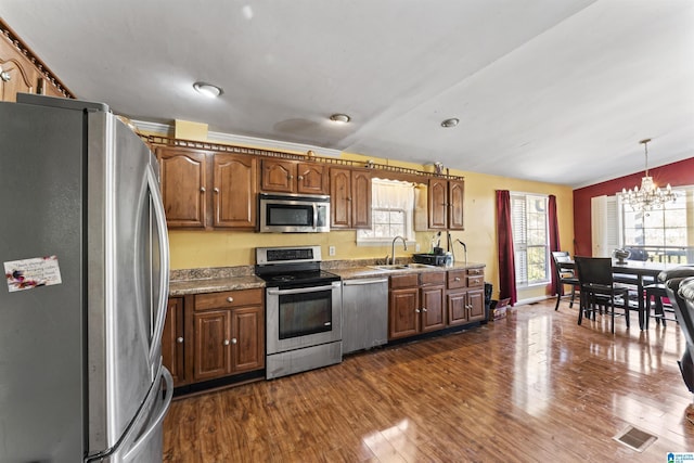 kitchen with dark wood-type flooring, stainless steel appliances, sink, hanging light fixtures, and a notable chandelier