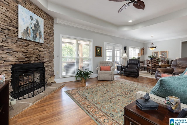 living room with french doors, ceiling fan, hardwood / wood-style flooring, crown molding, and a stone fireplace