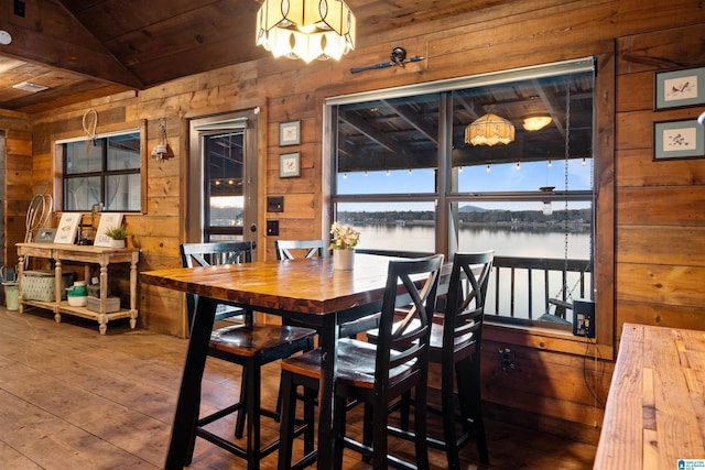 dining space featuring wood ceiling, a water view, wooden walls, and lofted ceiling