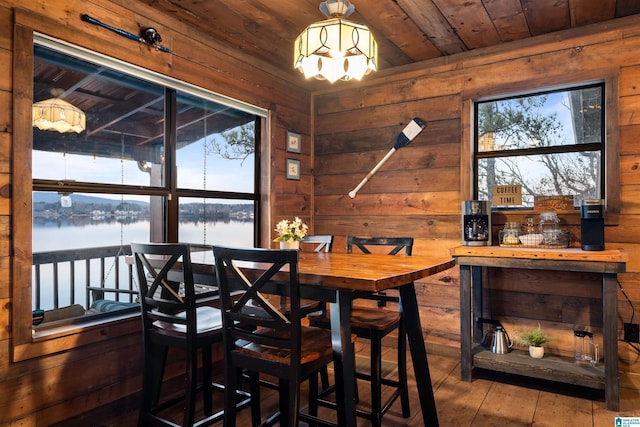 dining area with a chandelier, wooden walls, wooden ceiling, wood-type flooring, and a water view