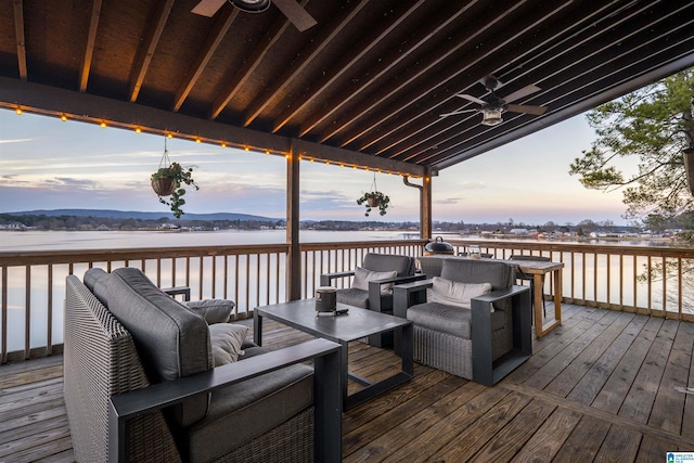 deck at dusk with an outdoor living space, ceiling fan, and a water view