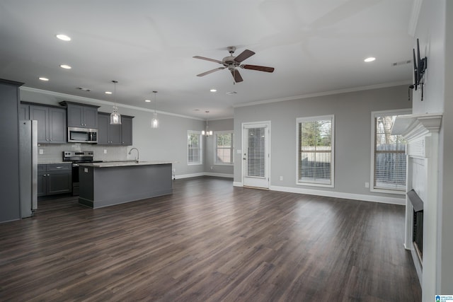 unfurnished living room with ornamental molding, ceiling fan with notable chandelier, plenty of natural light, and dark wood-type flooring