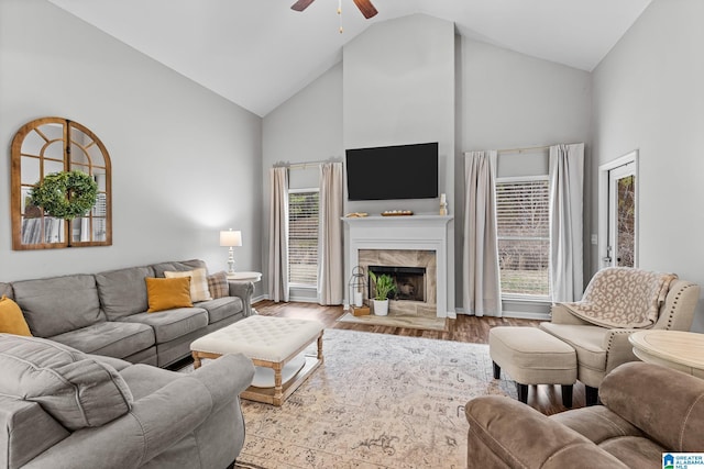 living room featuring a healthy amount of sunlight, a fireplace, high vaulted ceiling, ceiling fan, and light hardwood / wood-style flooring