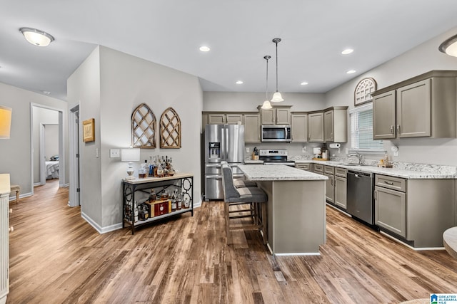 kitchen featuring hardwood / wood-style floors, a center island, a kitchen bar, stainless steel appliances, and hanging light fixtures