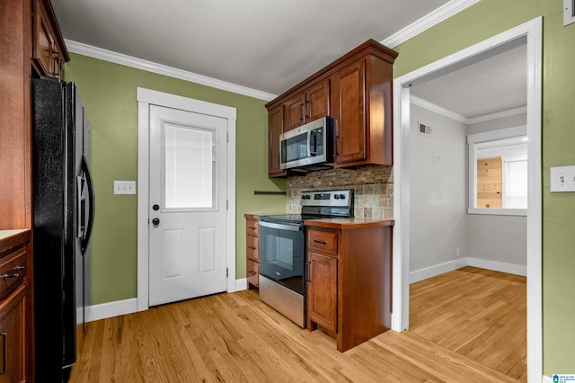 kitchen with appliances with stainless steel finishes, ornamental molding, backsplash, and light hardwood / wood-style flooring