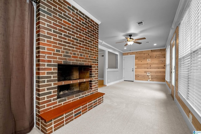 carpeted living room featuring ornamental molding, ceiling fan, wood walls, and a fireplace