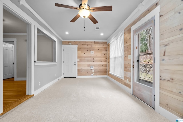 empty room with light carpet, wood walls, ornamental molding, and ceiling fan