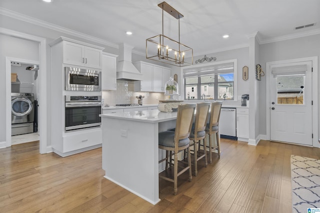 kitchen with custom exhaust hood, stainless steel appliances, washer / dryer, a kitchen island, and white cabinetry