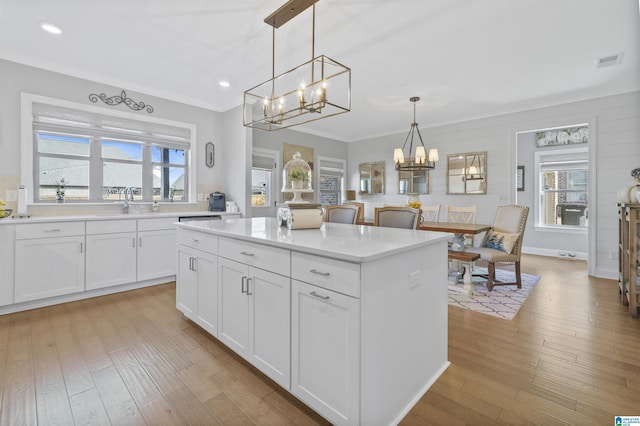 kitchen with a center island, light wood-type flooring, white cabinetry, and hanging light fixtures