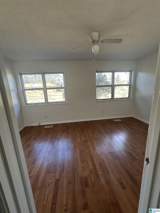 unfurnished room featuring ceiling fan, a textured ceiling, dark hardwood / wood-style flooring, and a healthy amount of sunlight