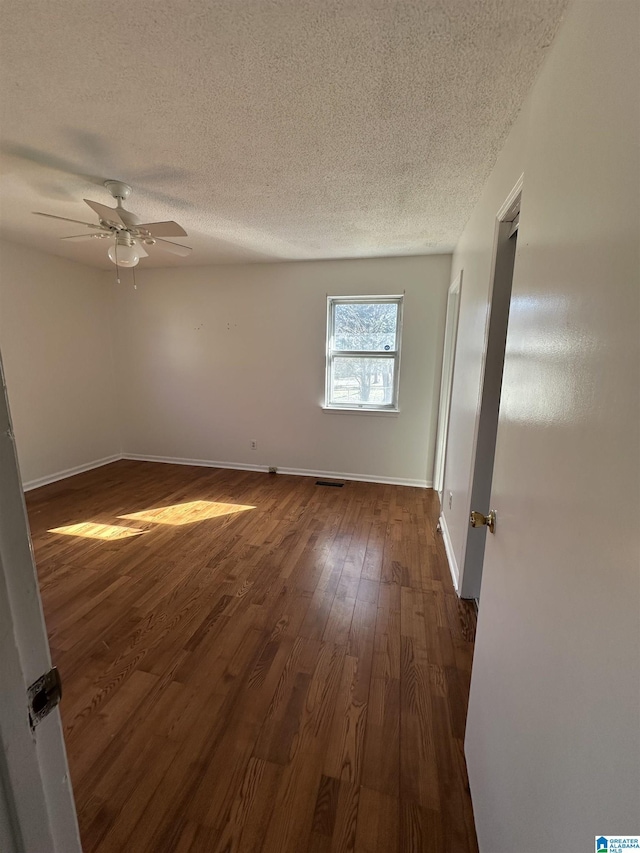 unfurnished room with a textured ceiling, dark wood-type flooring, and ceiling fan