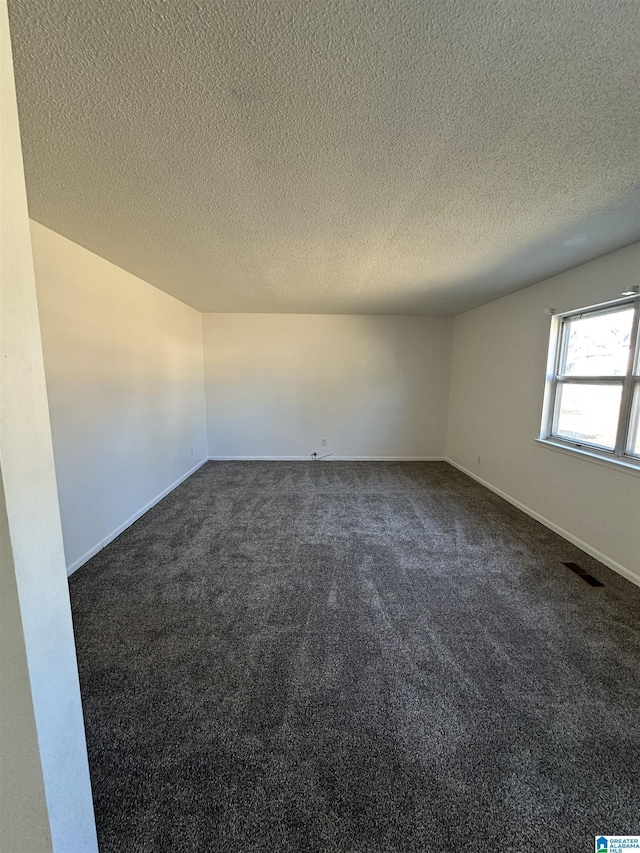 empty room with a textured ceiling and dark colored carpet