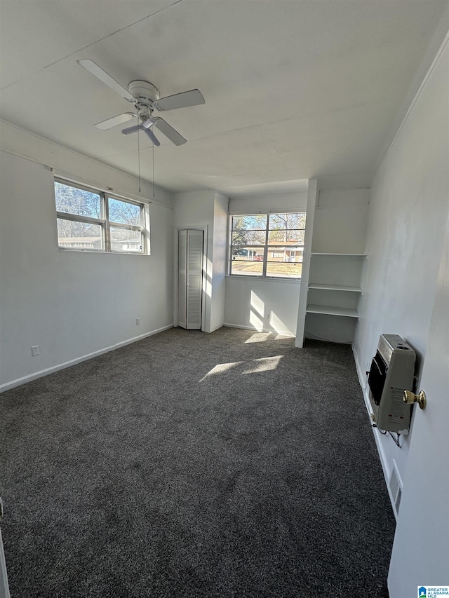 empty room with heating unit, ceiling fan, plenty of natural light, and dark carpet