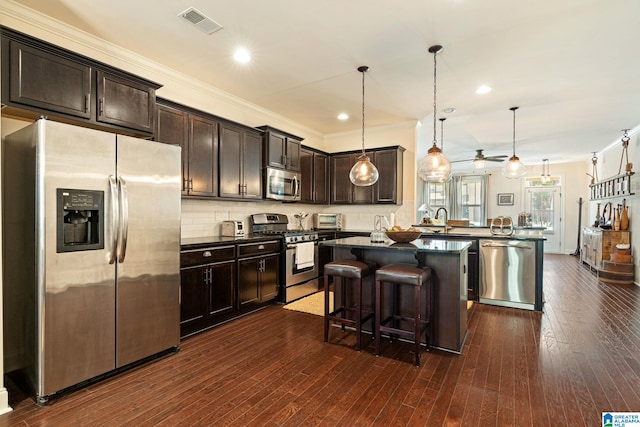 kitchen featuring backsplash, pendant lighting, kitchen peninsula, appliances with stainless steel finishes, and a breakfast bar area