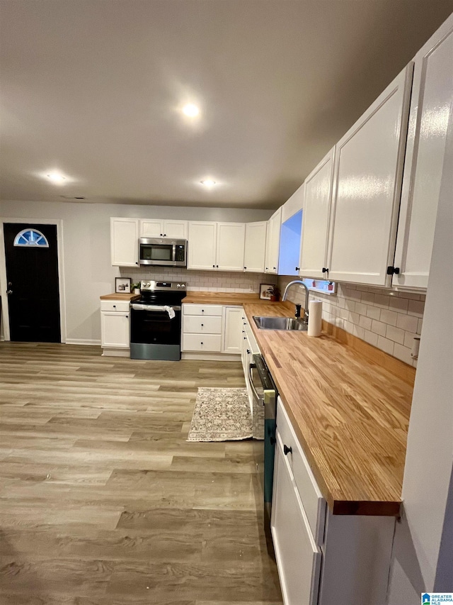 kitchen with white cabinets, appliances with stainless steel finishes, sink, light wood-type flooring, and butcher block countertops