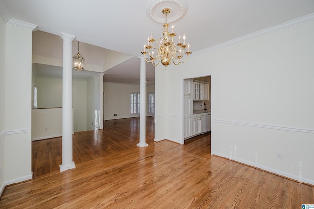 unfurnished dining area featuring ornate columns, ornamental molding, light wood-type flooring, and a notable chandelier