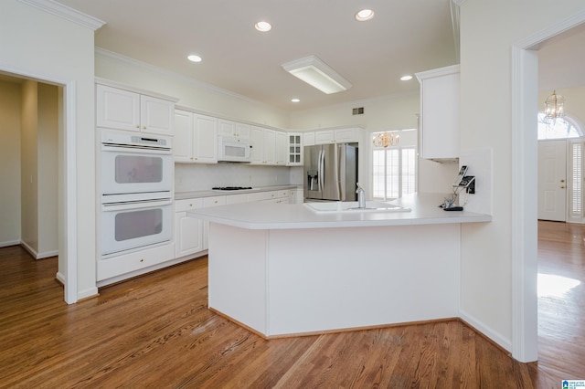 kitchen featuring hardwood / wood-style floors, white appliances, white cabinets, sink, and kitchen peninsula