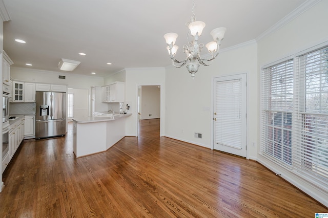 kitchen with kitchen peninsula, stainless steel fridge, tasteful backsplash, a notable chandelier, and white cabinetry