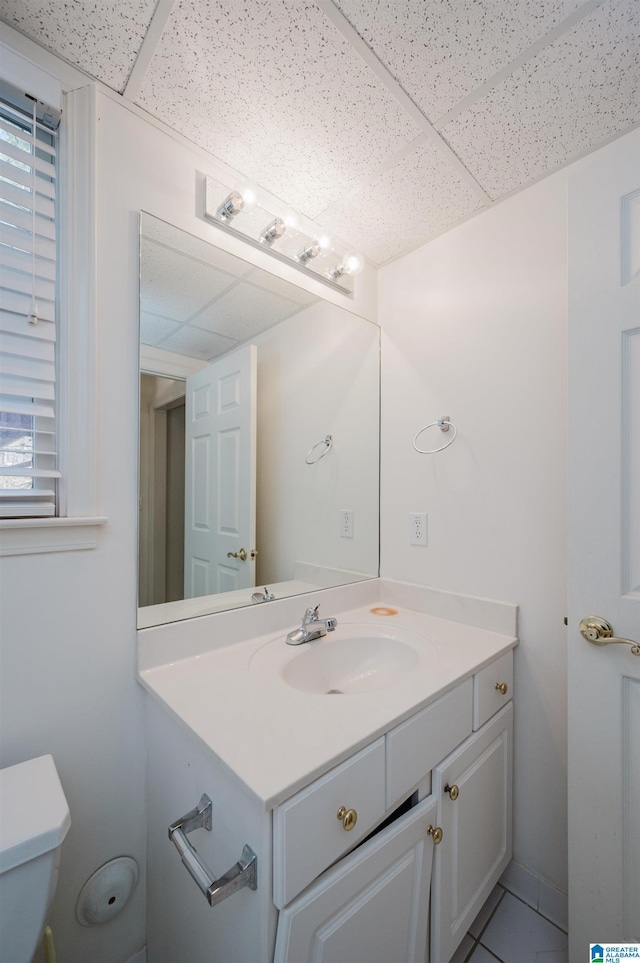 bathroom with toilet, vanity, tile patterned floors, and a drop ceiling