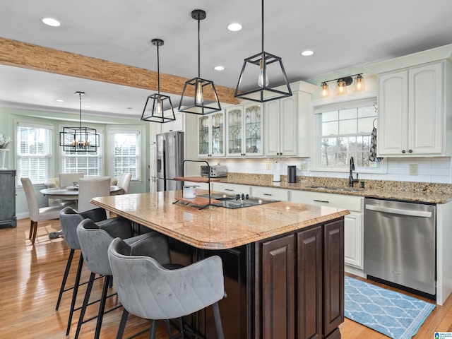 kitchen with stainless steel appliances, sink, white cabinetry, light stone counters, and a kitchen island