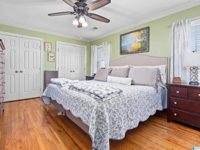 bedroom with ceiling fan, two closets, crown molding, and hardwood / wood-style flooring