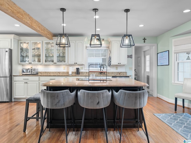 kitchen featuring tasteful backsplash, white cabinetry, stainless steel refrigerator, beamed ceiling, and sink