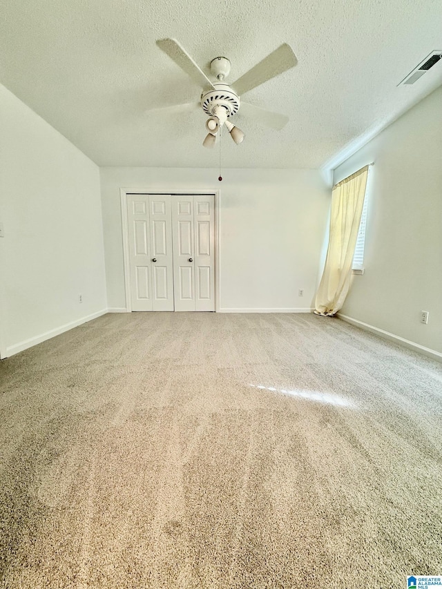 unfurnished bedroom with carpet flooring, ceiling fan, a textured ceiling, and a closet