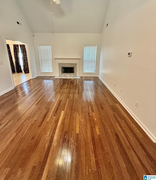 unfurnished living room featuring a premium fireplace, wood-type flooring, ceiling fan, and high vaulted ceiling