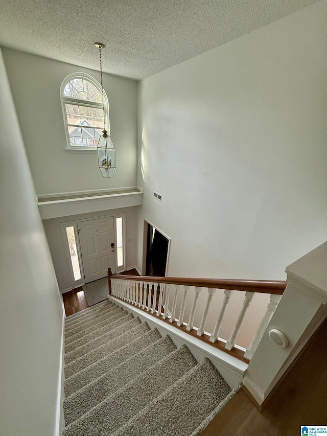 stairs with a chandelier, a textured ceiling, and hardwood / wood-style flooring