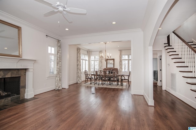 living room featuring crown molding, dark hardwood / wood-style floors, a tiled fireplace, and ceiling fan with notable chandelier