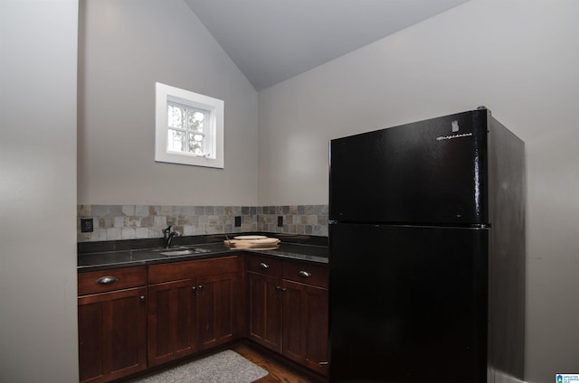 kitchen featuring lofted ceiling, sink, hardwood / wood-style flooring, black fridge, and decorative backsplash