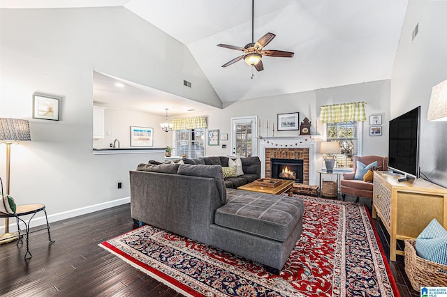 living room featuring ceiling fan with notable chandelier, a brick fireplace, a wealth of natural light, and dark wood-type flooring