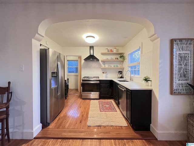 kitchen featuring sink, wall chimney exhaust hood, stainless steel appliances, tasteful backsplash, and light hardwood / wood-style flooring