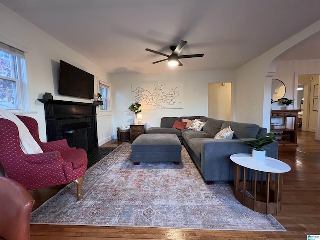 living room featuring ceiling fan, a fireplace, and dark wood-type flooring