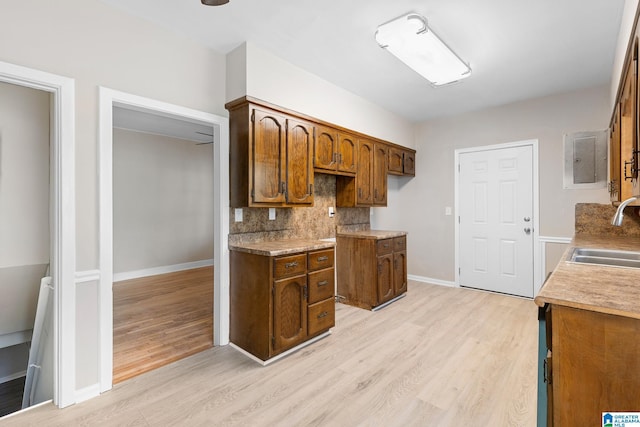 kitchen with electric panel, light wood-type flooring, backsplash, and sink