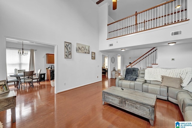 living room with ceiling fan with notable chandelier, wood-type flooring, and a high ceiling