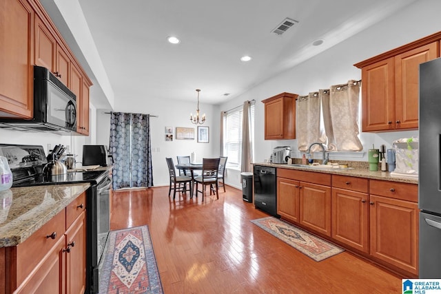 kitchen with pendant lighting, black appliances, sink, a notable chandelier, and light stone counters