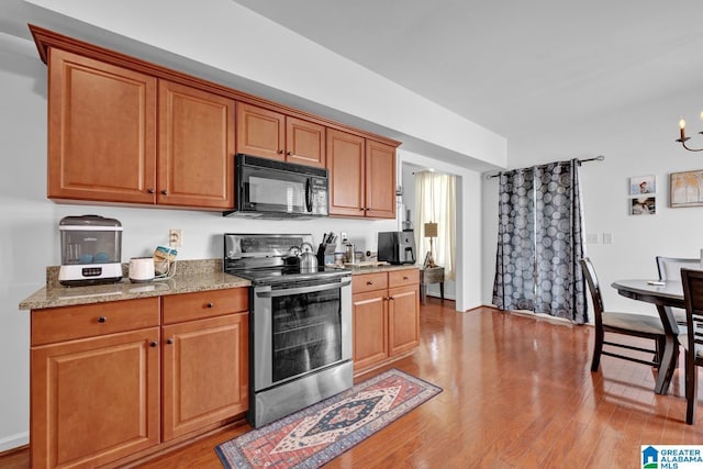 kitchen with electric range, light hardwood / wood-style flooring, light stone counters, and a notable chandelier