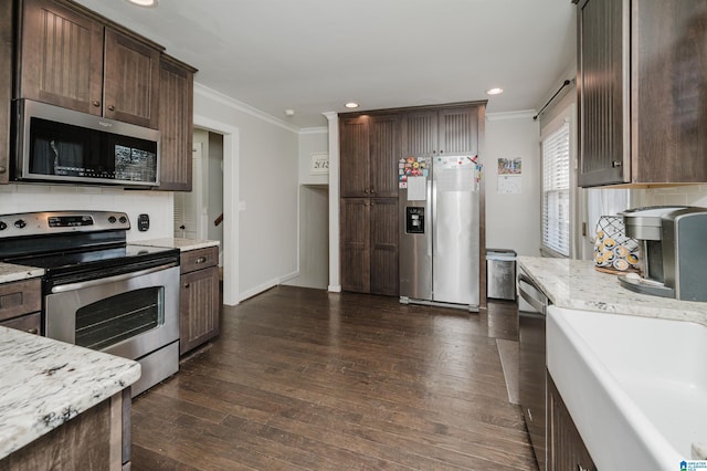 kitchen with dark wood-type flooring, light stone countertops, stainless steel appliances, crown molding, and dark brown cabinets