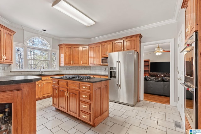 kitchen featuring ceiling fan, stainless steel appliances, decorative backsplash, a kitchen island, and ornamental molding