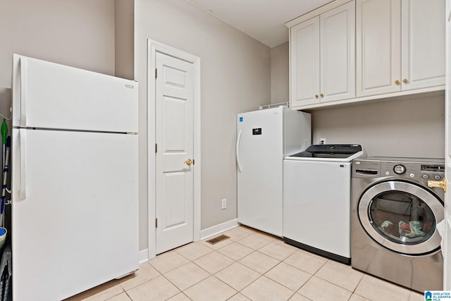 clothes washing area with light tile patterned flooring, cabinets, and washing machine and clothes dryer