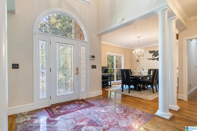 foyer entrance featuring ornate columns, a wealth of natural light, a chandelier, and ornamental molding