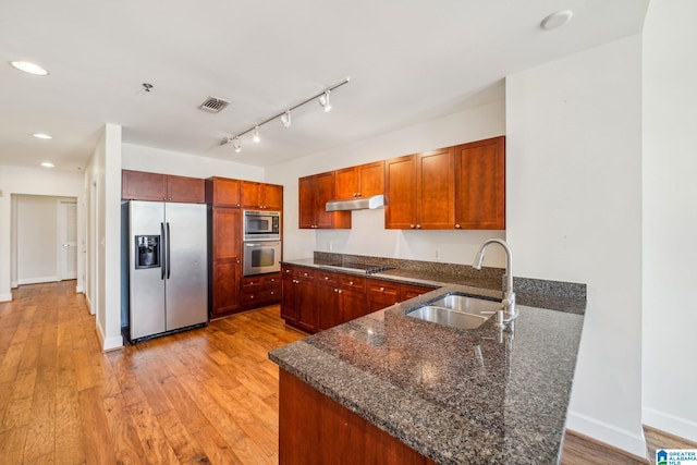 kitchen with kitchen peninsula, light hardwood / wood-style flooring, appliances with stainless steel finishes, dark stone countertops, and sink