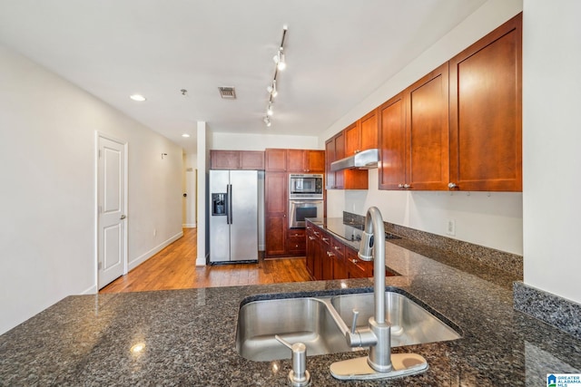 kitchen with dark stone countertops, appliances with stainless steel finishes, track lighting, light wood-type flooring, and sink